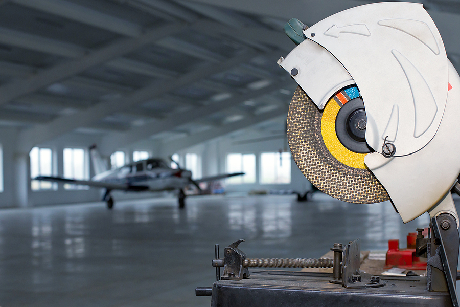 Circular saw in front of small single prop engine aircraft plane parked inside workshop hangar with opened door at aerodrome. Maintenance of private ultralight